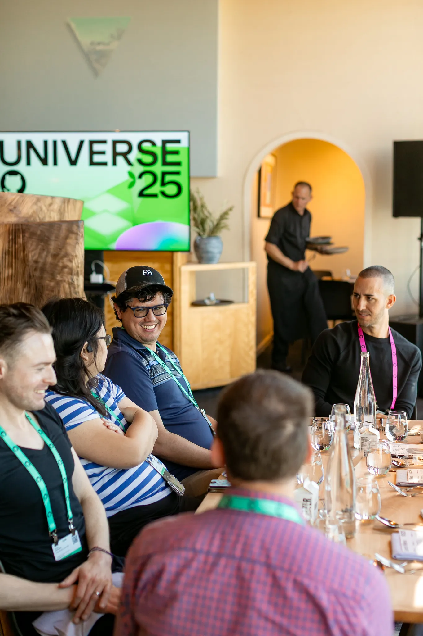 A group of attendees sitting at a table. A screen with Universe 25 logo in the background.